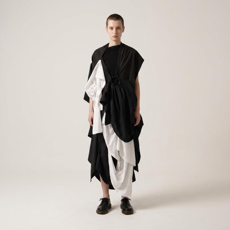 Model in einem geschichteten schwarz-weißen Ensemble aus drapiertem Stoff vor neutralem Hintergrund.